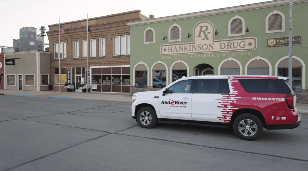 A Red River Communications SUV parked in front of Hankinson Drug store in a small town.